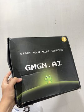 A hand holds a black package displaying "START YOUR VIBE TRADING" and "GMGN.AI" alongside a green frog character, which aligns with the post's reference to @gmgnai and the frustrations of high trading taxes.