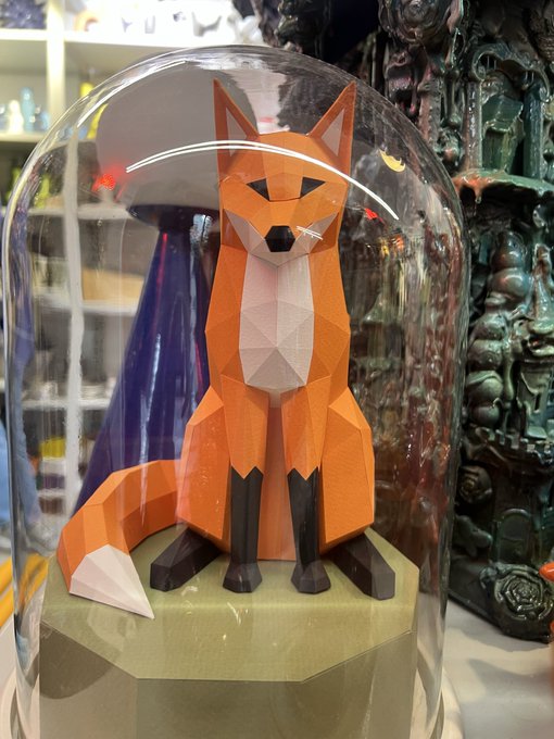 A geometric low-poly orange and white fox figurine sits on a green base inside a clear glass dome.