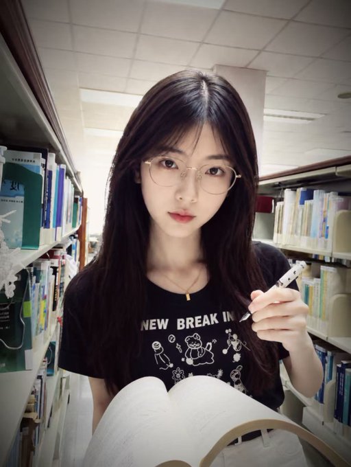 A young woman with long dark hair and glasses stands in a library holding a pen and open book, wearing a black t-shirt with "NEW BREAK" text visible, fitting the post's call for honest mutual follows from fellow dedicated users.