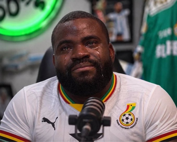 A tearful man wearing a Ghana Football Association jersey sits at a microphone in front of a green-lit '60%' sign and framed photos.