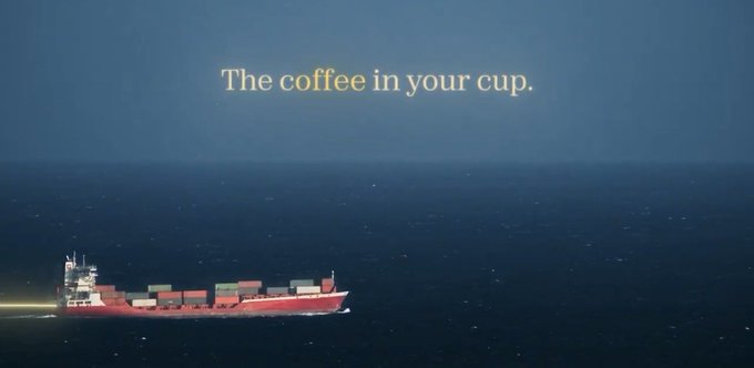 A large red cargo ship sails across a dark blue ocean with the text 'The coffee in your cup.' overlaid in yellow serif font.
