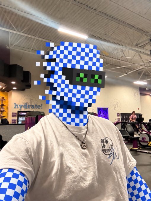A person in a gym wears a white t-shirt with a cartoon skull design and a blue-and-white checkered 3D avatar mask overlay.