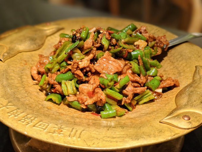 A close-up photo of a Chinese stir-fry dish featuring sliced meat and green peppers served on a decorative brass or gold-colored platter with Chinese characters embossed on it.