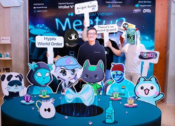 The image shows a man wearing glasses and a Hyperliquid hoodie posing at an immersive event booth featuring cartoon-themed mascots, a Nescafé sign, and signage reading "Hypio World Order" with social media handles like @HypioBase. The scene reflects the post's theme of a memorable Hyperliquid event in Vietnam, highlighting the strong visual identity and creative branding that made it stand out a year later.