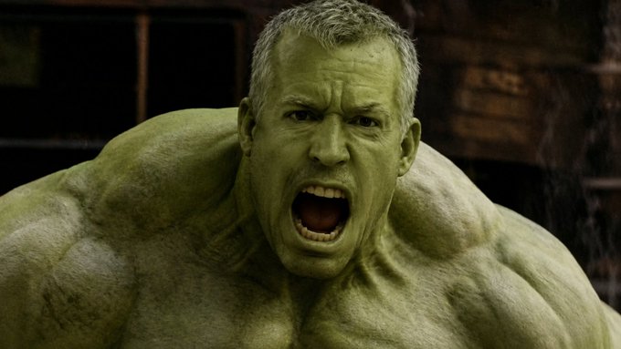 An image shows the Hulk, a large green muscular humanoid, roaring aggressively with his mouth wide open in what appears to be a dimly lit industrial setting.