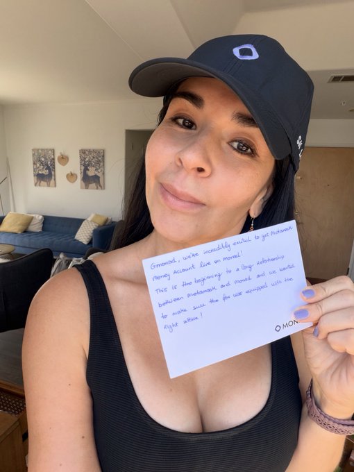 A woman wearing a navy baseball cap and black top holds a handwritten note thanking her Instanet money account for being crucial, with text mentioning 'beginning to a large path' and making her eyes 'the first eight action'.