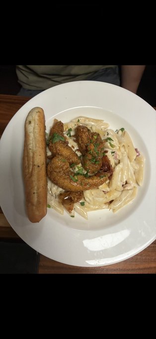 A plate of food featuring a sausage, fried chicken pieces, and penne pasta in a creamy sauce garnished with herbs, served on a white dish.