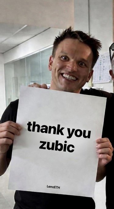 A man smiling broadly while holding up a printed sign that reads 'thank you zubic' with the LemzETH logo in the bottom right corner.