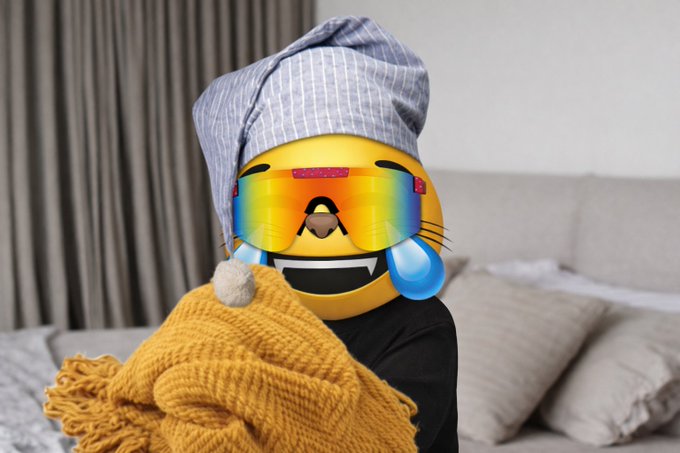 A person wrapped in a yellow blanket wearing a striped hood, with their face covered by a large laughing-crying emoji wearing rainbow sunglasses.