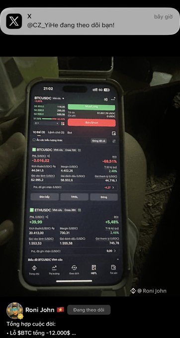 A person holds up a smartphone displaying a trading app (likely Binance) showing a BTC/USDC short position with a -69.55% loss and ETH/USDC positions. The visible account details, including the liquidation price and margin ratios, directly illustrate the post's concern about the brother's long $BTC position at 62k with a liquidation level in the 44k range.