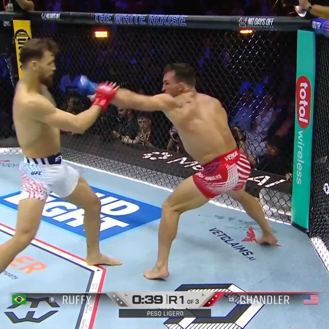 The image shows two boxers fighting in a ring, with one boxer wearing red shorts and the other wearing white shorts. The fighter in red shorts appears to be dominating the fight by delivering a powerful kick towards his opponent's face. Both boxers are wearing gloves as part of their protective gear during the match. The post about the fight is titled "BYE OFF TO SLEEP Maurício Ruffy dominates Chandler with a powerful kick and finishes the fight in the first round #UFCWhiteHouse". This suggests that the fighter from the red shorts has won the bout, while the fighter from the white shorts has lost.