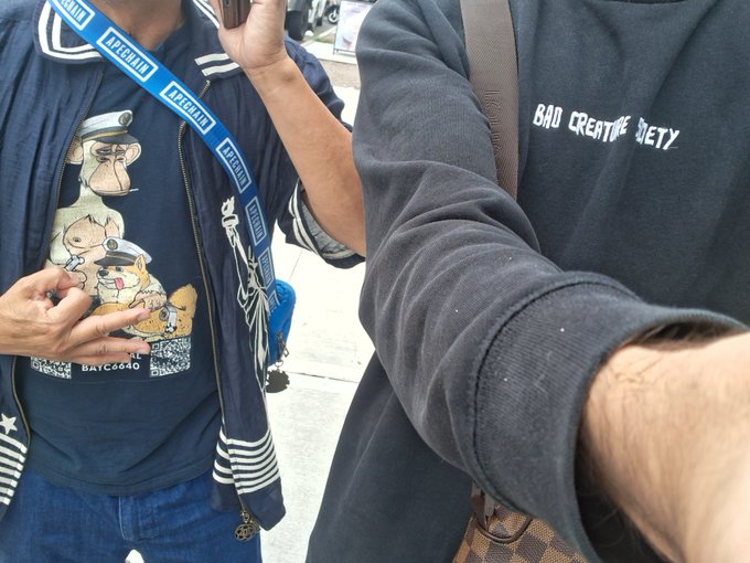 Two friends pose together at an IRL community meetup, with one wearing a "BADC Creature Society" sweatshirt and the other sporting a "City of Stonks" graphic tee featuring nautical-themed cartoon dogs, complemented by a blue lanyard. The casual street-style fits and friendly selfie capture the laid-back vibe of the "City of Stonks" community gathering tagged with @JaysonCrypto.