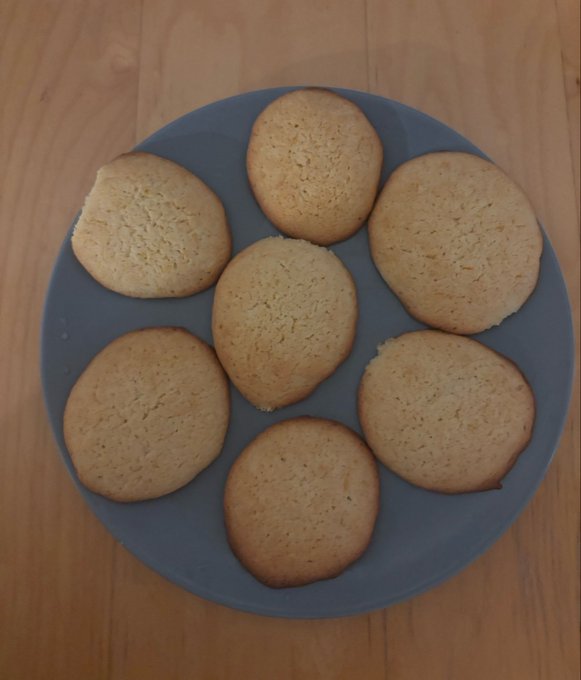 Seven golden-brown round cookies arranged on a blue ceramic plate, sitting on a wooden surface.