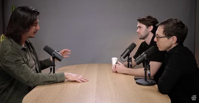 Three men sit at a podcast/interview table with professional microphones, suggesting a tech or finance discussion setup.