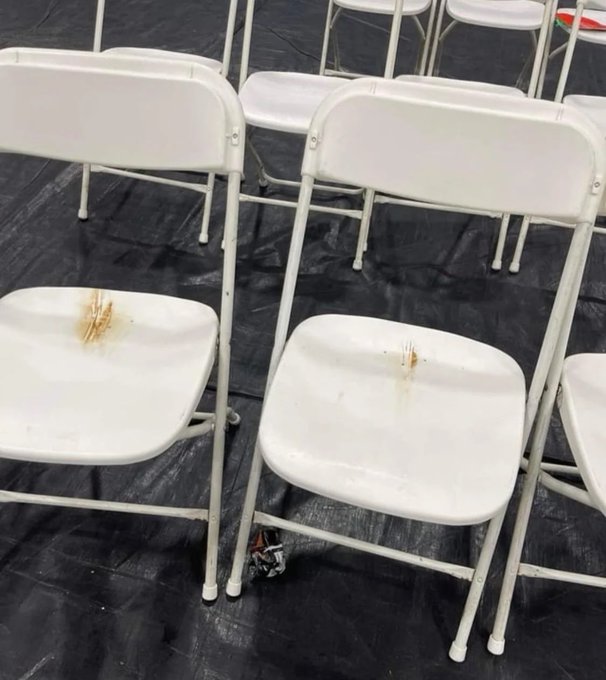 Several dirty, stained white folding chairs sit on a black tarp, with brownish burn or liquid marks visible on the plastic seats. The grimy condition of the seating humorously underscores the post's sentiment about a disappointing crypto conference experience.