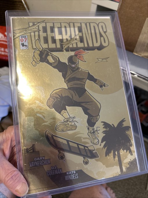 A hand holding a gold-foil cover comic book titled 'KEELFRIENDS Issue 07', featuring a ninja character on a skateboard, with creator names 'GARY VAYNERCHUK, DJ COFFMAN, KATE WINDELS' at the bottom.