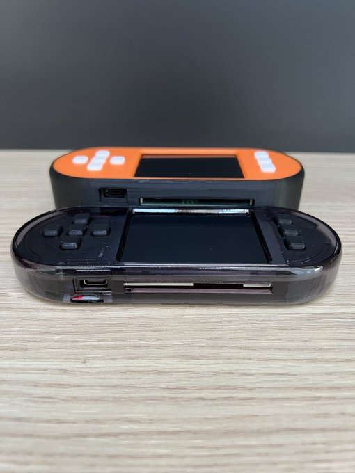 Two SeedSigner Bitcoin signing devices are displayed stacked on a wooden surface, with an orange-cased unit on top and a translucent-cased unit below featuring a large screen, buttons, and visible ports including a card slot. The image showcases different SeedSigner hardware variants being referenced in the post, likely highlighting the big-screen models with smartcard capabilities.
