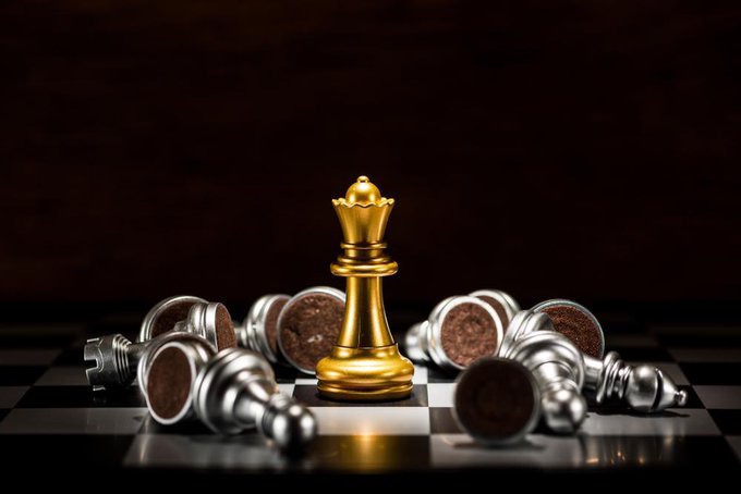 A golden king chess piece stands upright and victorious while silver pawns lie fallen around it on a chessboard.