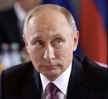 Vladimir Putin, with a stern expression, is shown in a close-up portrait wearing a dark suit and tie, against a blurred background that appears to include a Russian flag—visually tying him to the accompanying news about Russia's Ministry of Finance beginning to pay state employees in a central bank digital currency (CBDC).