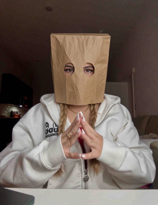 A person with braided hair wears a brown paper bag over their head with eye holes cut out, hands clasped in front of them, wearing a white hoodie featuring a panda graphic and the partially visible text "BOG PREMIUM," visually reinforcing the post's message that "the bag STAYS on $ZCAT" through the literal commitment to keeping the bag on.