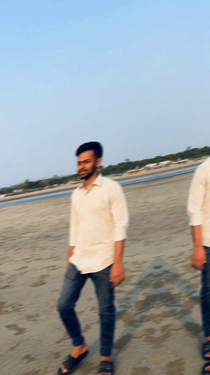 The image shows a man walking along a beach wearing a white shirt and blue jeans. The photo has been edited, giving two different versions of the same person. One version features the man with his arms crossed, while the other shows him holding a surfboard. Both images have a grainy appearance, suggesting that they were taken using a low-quality camera or image editing software.