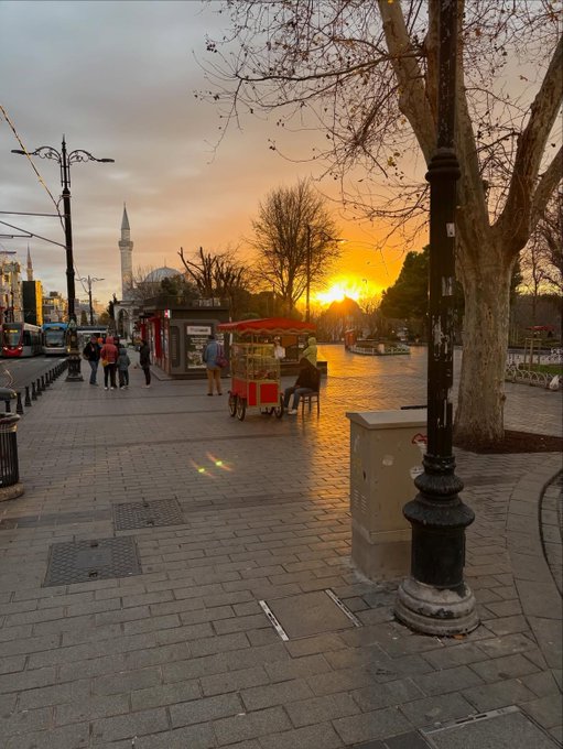 A sunset over Istanbul with the Bosphorus, a distant minaret, and a simit cart glowing warmly under the dusk sky—capturing the peaceful "GM" (Good Morning) energy of the city awakening.