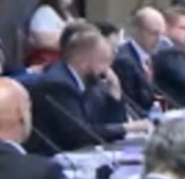 A blurry image captures Sergey Nazarov of Chainlink seated at a formal CFTC meeting, focused intently on taking notes alongside other attendees. The scene aligns with the post highlighting Nazarov's active participation and Chainlink's presence at the regulatory discussion.