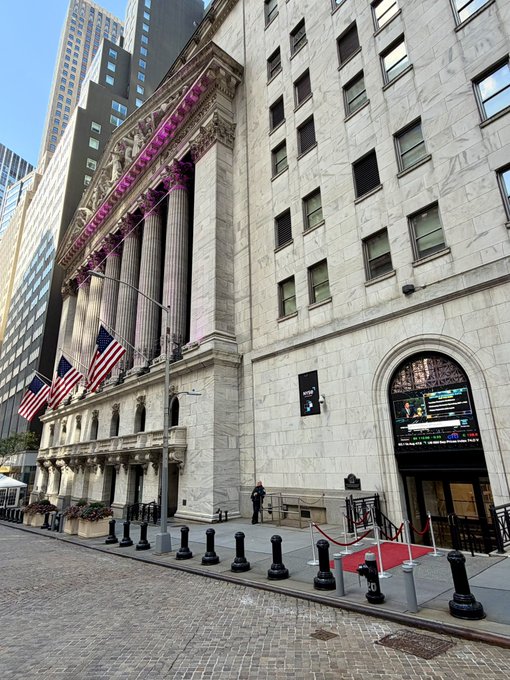 The New York Stock Exchange stands prominently on Wall Street, where a few Suits in suits can be seen near the entrance—perhaps discussing the recent buzz around $OKLO.