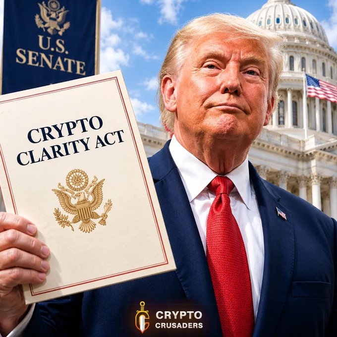 Donald Trump stands outside the U.S. Capitol holding a document titled "CRYPTO CLARITY ACT," with a "U.S. SENATE" banner behind him and a "CRYPTO CRUSADERS" logo in the corner.