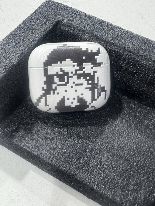 An AirPods Pro case featuring a pixelated Normie character design rests on a dark foam display tray. The image showcases one of the lowest minted Normie NFTs from the @normiesART collection, presented as a prized collectible "grail" piece.