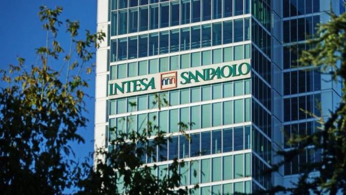 A modern glass office building displays the green 'INTESA SANPAOLO' bank signage near the top, framed by tree branches in the foreground.
