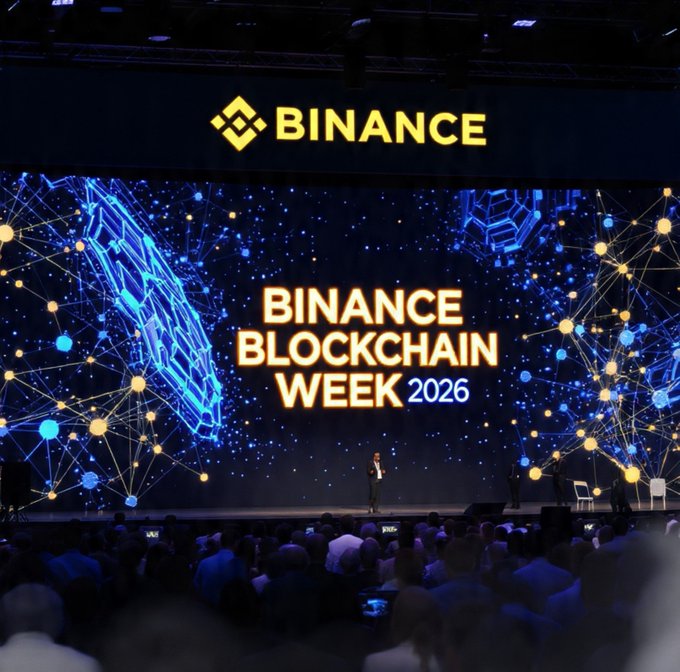 A speaker addresses a large audience at Binance Blockchain Week 2026, with the event's title and Binance logo prominently displayed on a massive digital screen behind the stage. The image visually reinforces the post's announcement of the conference as a key gathering for the crypto and blockchain industry.