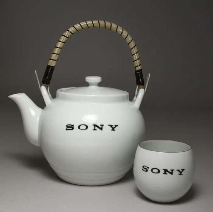 A white ceramic teapot with a woven handle and a matching teacup, both featuring the 'SONY' logo in black text, sit against a gray background.