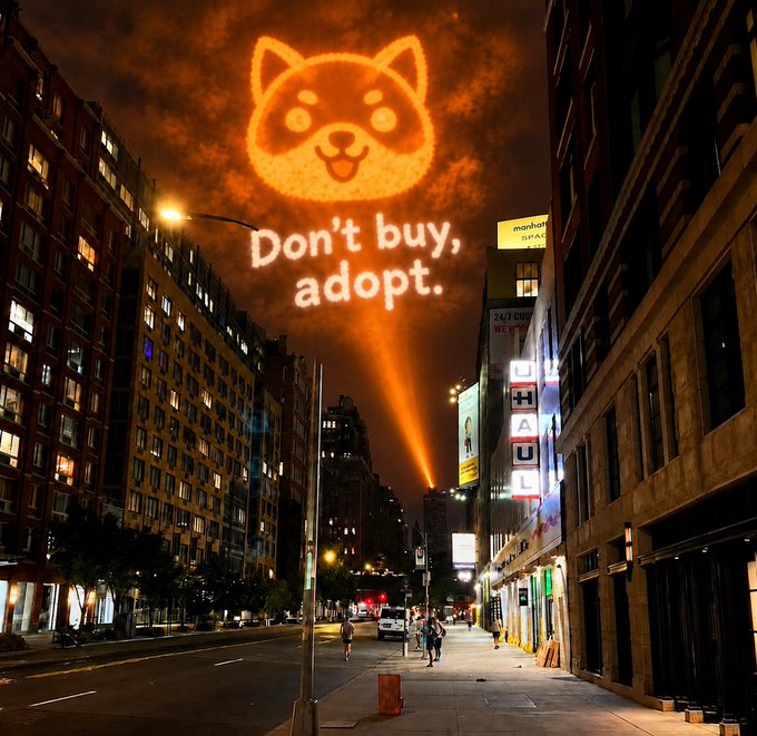A nighttime city street features a giant glowing Shiba Inu projection in the sky above the slogan “Don’t buy, adopt,” alongside a vertical “U-HAUL” sign. The adoption message provides a hopeful, playful new “hero” for the city.
