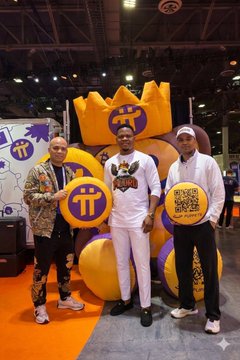Three men posing at a Pi Network (π) crypto event booth, with two holding Pi Network logos and one holding a QR code placard, standing next to a large mascot figure wearing a crown.