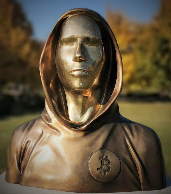 A bronze bust of a hooded figure with a Bitcoin logo medallion on the chest, depicted as a "fortune teller" or oracle. The statue humorously represents the post's mocking prediction that Bitcoin will drop below $55,000 by October, casting the forecaster as a mystical figure whose prophesies are not to be trusted.