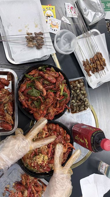 The image shows a table filled with various dishes of food, including a large bowl of crayfish. The table also has several bottles and cups scattered around, along with some chopsticks. A person wearing gloves can be seen near the center of the scene, possibly preparing or serving the food. The post mentions that it is Crypto Survival Plan Day, which could suggest that the person might have used a Bitcoin wallet to purchase their meal.