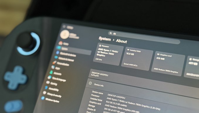 A close-up of a Steam Deck handheld gaming console screen displays the 'System > About' menu, showing device specs including an AMD Ryzen 7 7840U processor, 16.0 GB RAM, and AMD Radeon 780M Graphics for a device named 'DESKTOP-1NLVD7DU'.