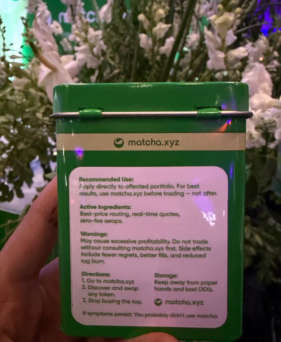 The image shows a person holding a green tin box containing matcha tea, which has a label attached to it. The label provides information about the product, including its recommended usage, active ingredients, storage instructions, and warnings. The person's hand is visible in front of the box, indicating that they are holding or displaying the product for others to see.