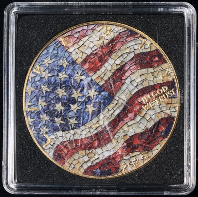 A close-up of a silver coin featuring a colorful mosaic American flag design and the text 'LIBERTY,' 'IN GOD WE TRUST,' and '2025,' encased in a clear protective holder.