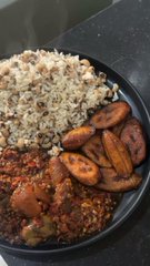 A black bowl filled with a meal consisting of brown rice, sliced sausage, and a bean stew with tomatoes, served on a dark surface.