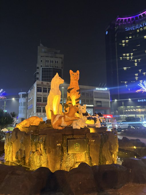 A nighttime photo shows an illuminated sculpture of dogs perched on a rocky base in Borneo, with a Sheraton hotel building and "SOLARVEST" signage visible in the background, capturing the vibrant atmosphere of the SuperteamMY Solana startup village event.
