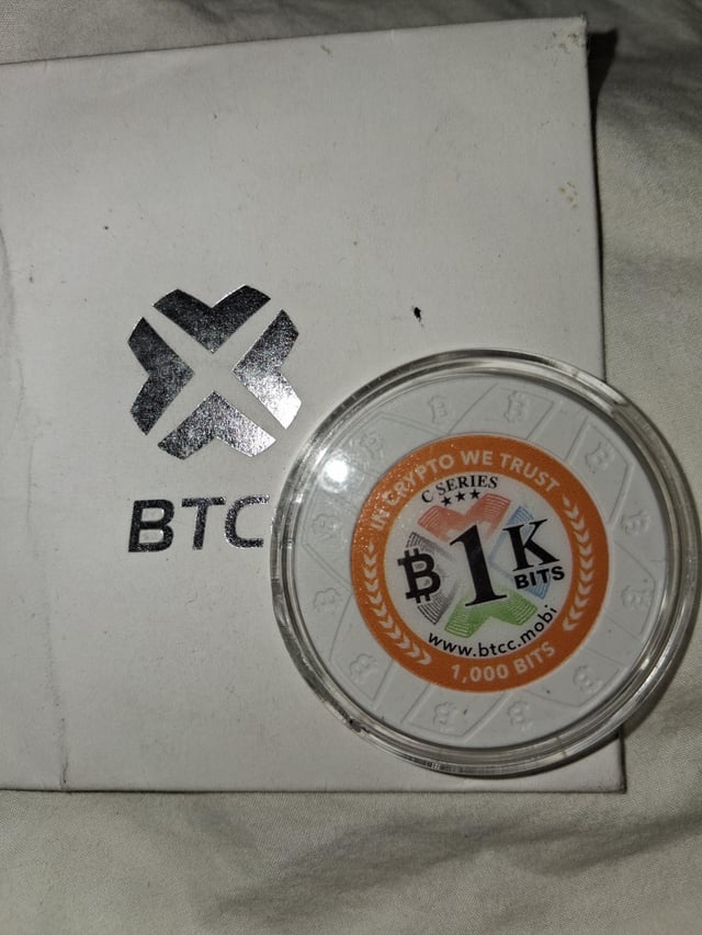 A commemorative "1K BITS" Bitcoin token from the "C Series" (1,000 bits) issued by BTCC (btcc.mobi) rests on its white BTCC-branded envelope, serving as a collectible piece of cryptocurrency memorabilia.