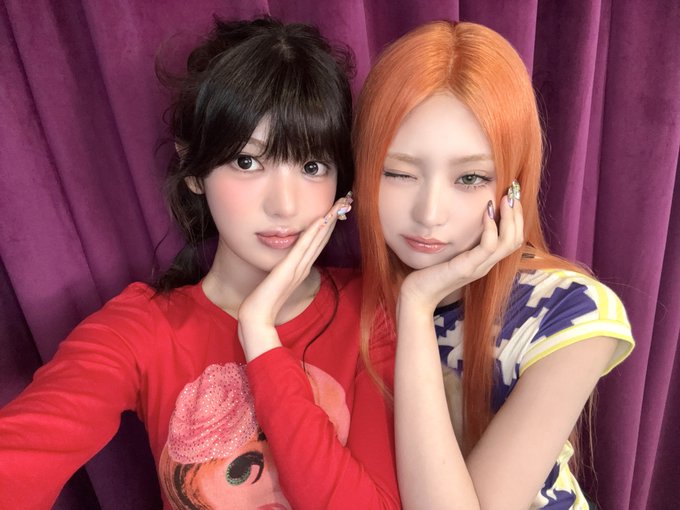 Two young women pose closely together for a selfie against a purple curtain backdrop, one with dark hair in a red graphic long-sleeve top and the other with vibrant orange hair winking while resting her cheek on her hand in a colorful patterned shirt. The Korean hashtags "오늘도 함수즈이지" (meaning "today is also a fun day too"), along with #KiiiKiii, #키키, #SUI, and #수이, suggest this is a playful fan post or promotional image featuring members Kiki and Sui from the K-pop group KiiiKiii.