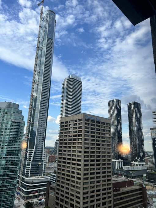A daytime cityscape view showing several modern skyscrapers, including the Fairmont Royal York hotel, under a partly cloudy sky.