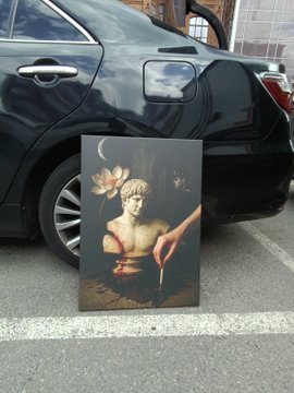 A framed classical-style painting of a cherub holding a lotus flower and a candle, leaning against a black car in a parking lot.