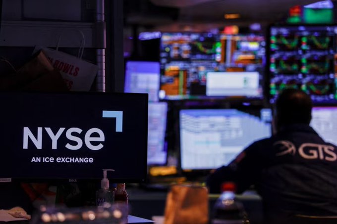 A trader in a GTS jacket works at a multi-monitor trading station at the New York Stock Exchange (NYSE), with a Dell display showing the "NYSE - An ICE Exchange" logo in the foreground. The image visually reinforces the post's message by depicting traditional Wall Street trading floors and stock exchanges—not crypto-native platforms—as the real force behind BTC and ETH price movements through interest rates, the dollar, and broader market dynamics.