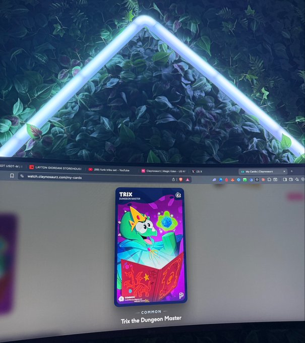 A computer monitor displaying a 'Trix' digital collectible card called 'Trix the Dungeon Master' from Claynosaurz Magic Gate, viewed against a backdrop of a neon triangle light and leafy wall.