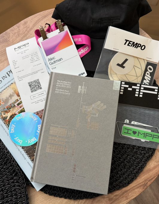 A collection of conference badges and materials, including one for 'Alec Gutman' from Visa and a 'Stripe' badge, sits on a table along with books and other swag.