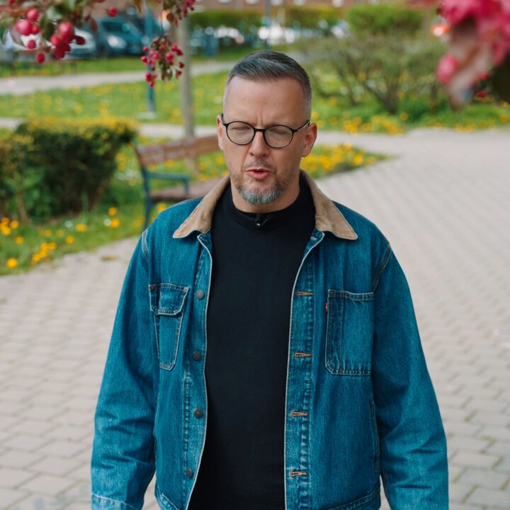 The image features a man wearing glasses and a blue denim jacket walking down a brick sidewalk with flowers blooming nearby. The man appears to be looking at something or someone off-camera, possibly contemplating his next move or decision. The text on the image reads "Only ~14 days left. Get your ticket and be there." This suggests that the event is approaching quickly, and the man might need to make a decision soon regarding whether he wants to attend the event or not.